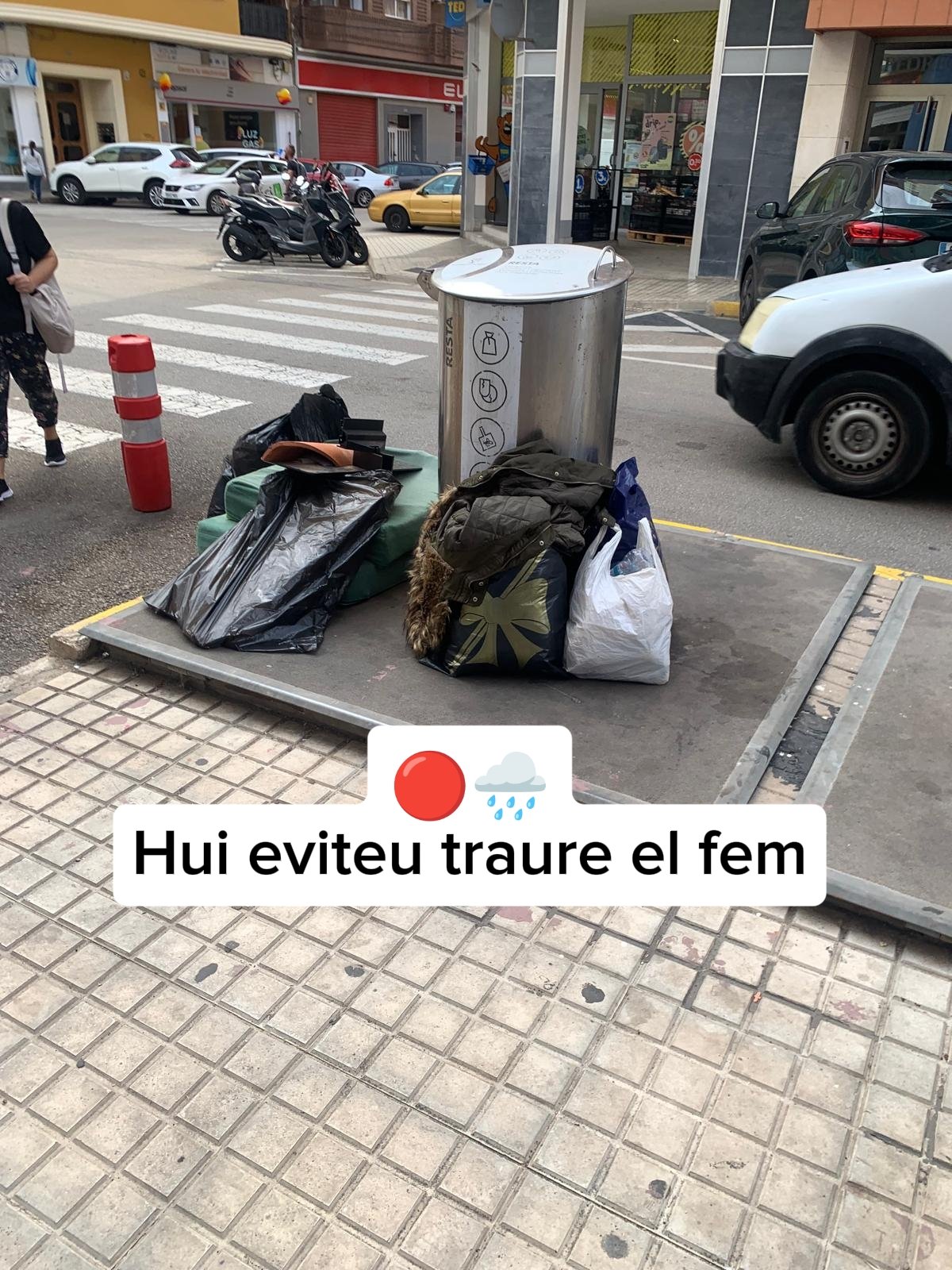 Bags of rubbish left beside a street waste bin in Dénia, with an overlay reading "Hui eviteu traure el fem" (Please do not put rubbish out today)